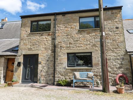 Exterior view of a stone house with two windows a door a blue bench with cushions and a plant pot at 24 Hauxley Links Low Hauxley near Amble