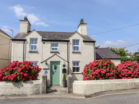 A two story house with a green door and red flowers in front at Bryn Peris in Moelfre