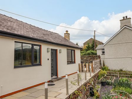 A house with a gray door and windows next to a garden with plants at Bryn Hyfryd in Harlech
