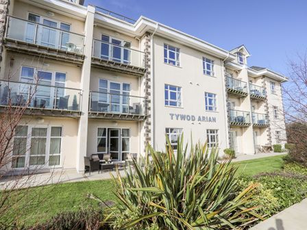 The exterior of a three story building with balconies and patio furniture at Y Gyfrinach in Morfa Nefyn