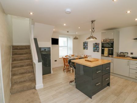 A kitchen and dining area with a carpeted staircase on the left and kitchen island in the center at Bryngolau in Morfa Nefyn