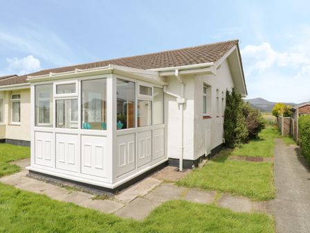 A white conservatory attached to a single story house with a tiled roof and a grass lawn at Hafod-y-Gors in Fairbourne