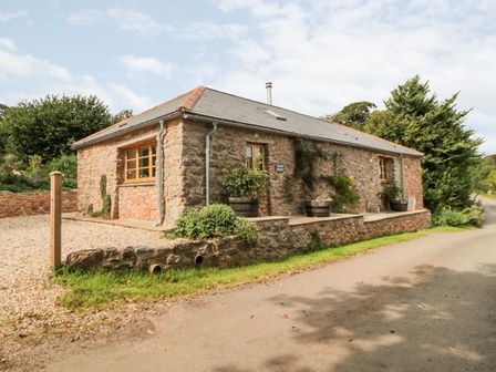 A stone building with wooden windows and plants outside along a gravel driveway at The Old Haybarn in Ipplepen