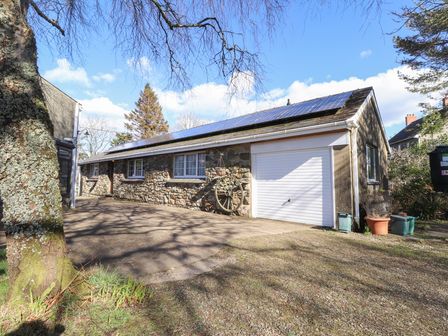 A stone house with solar panels on the roof and a white garage door surrounded by trees at Otter Cottage in Dinas Cross