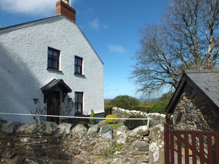 A white house with a brick chimney beside a stone wall and a wooden gate at Blaenpant Bach in Newport Pembrokeshire