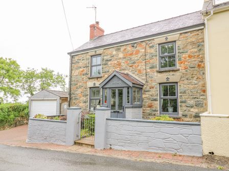 Stone house with gray framed windows and a gray porch with a gate and small brick driveway at Greenbanks in Dinas Cross Pembrokeshire