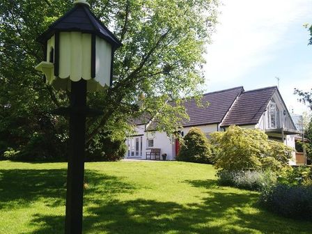 A garden with a birdhouse on a post and a house with a balcony and a red door at Pond Cottage in New Quay Ceredigion