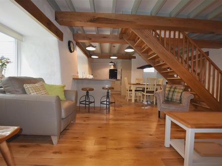 An open plan living area with a gray sofa, two bar stools, dining table with chairs under wooden stairs at The Old Farmhouse Kitchen in St Davids Pembrokeshire
