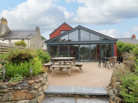 An outdoor patio with wooden and metal seating and a glass extension on a red house at Nevern House in Newport Pembrokeshire
