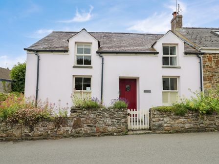 A two-story house with a red door and four windows surrounded by a stone wall and flowers at Panteg Cottage Newport Pembrokeshire