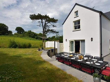 An outdoor dining table set with plates and cups on a patio next to a white house with a view of a grassy field at Gwelfor Newport in Newport Pembrokeshire