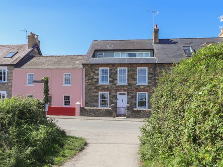 A stone house with white framed windows and a pink house next to it on a roadside at Neverndale in Newport Pembrokeshire
