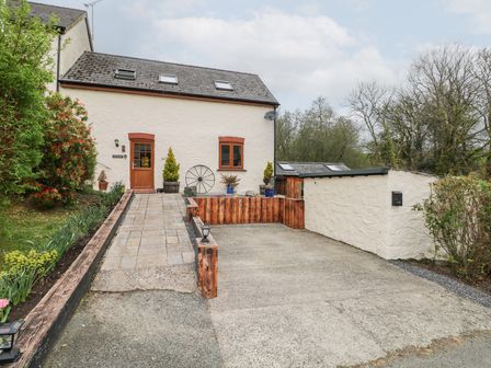 An exterior view of a house with a driveway and a paved pathway leading to a wooden door surrounded by plants and trees at Mill Barn Denant in Haverfordwest Pembrokeshire