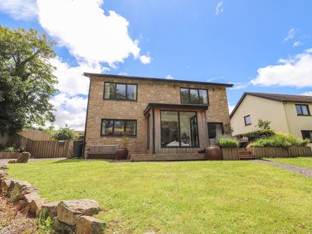 A two-story stone house with a grassy front yard and a wooden bench at Ty Cerrig in Newport Pembrokeshire