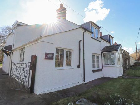 A white exterior of a cottage with windows and a metal gate at Meadowlands in Dinas Cross Pembrokeshire