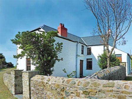 A white farmhouse with stone walls trees and a clear sky at Panteurig Farmhouse in Strumble Head Goodwick Pembrokeshire