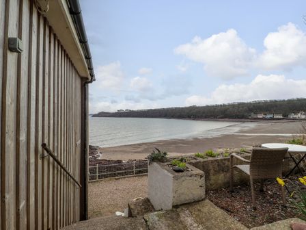 A waterfront view with a sandy beach trees and a small patio area with a chair and table at Blackrock Boathouse in Dale Pembrokeshire