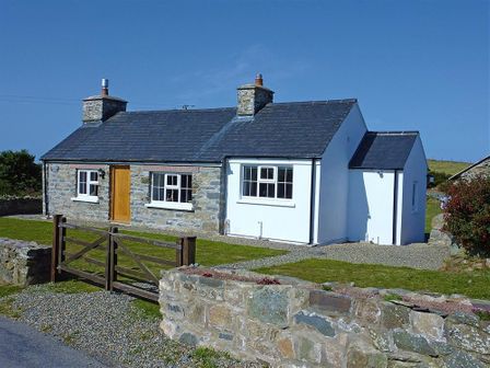 A stone and white cottage with a wooden gate and low stone wall at Gwndwn Gwyn in Trefasser Near Strumble Head