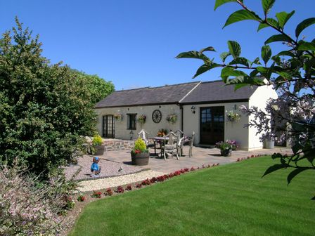 A garden with green lawn flowers and patio furniture outside a cottage at Y Stabl in Fishguard Pembrokeshire