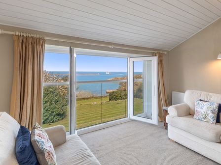 A living room with two sofas facing large glass doors opening to a view of the sea and garden at The Rock House in Fishguard Pembrokeshire
