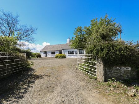 A white cottage with a slate roof behind a gravel driveway and open metal gates at Ty-Newydd Cottage in Nevern near Newport Pembrokeshire