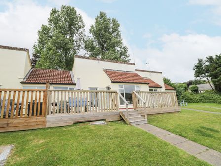 A bungalow with a wooden deck and outdoor furniture on a grassy lawn at 9 Manorcombe Bungalows in St Ann's Chapel near Callington