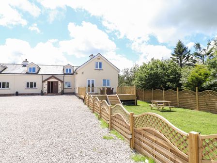 Exterior view of a house with a gravel driveway wooden fence and picnic table at Bryn Awel in Peniel near Denbigh