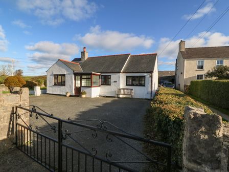 A white detached house with a black iron gate and a driveway at Penllwyn in Llanddona near Beaumaris