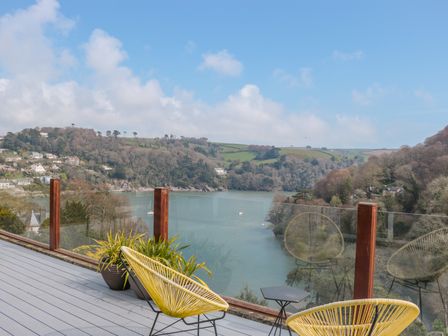 A balcony with yellow chairs and plants overlooking a river and hills at High Banks in Dartmouth