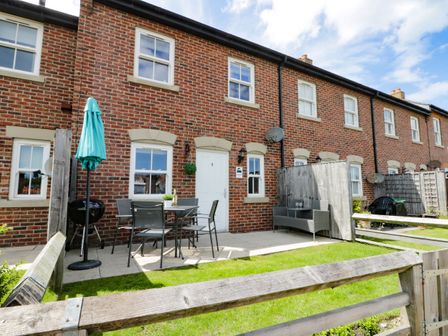 A patio area with outdoor furniture and a green umbrella in front of a brick row house at Harbour Walk in Whitby