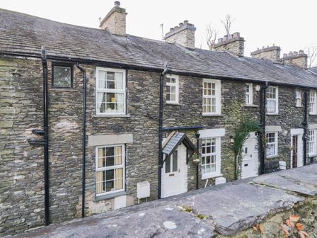 A row of stone cottages with white framed windows and doors behind a stone wall at Dalesway Cottage in Bowness-On-Windermere