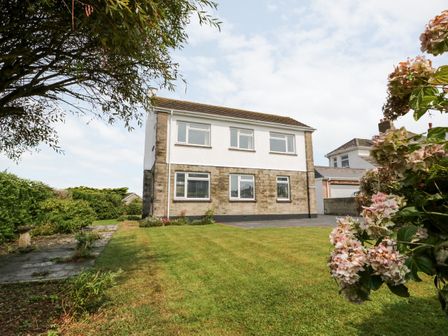A two-story house with a lawn and flowers in the garden at Awel-Y-Mor in Bude