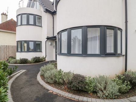 The exterior of a modern house with curved walls dark framed windows a paved pathway and garden beds at Flat 2 38 Preston Road Weymouth