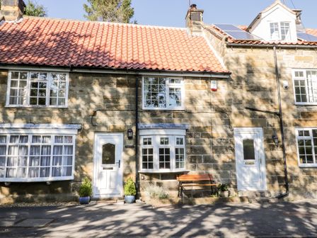 Stone cottage with white doors and windows and a bench outside at Parva in Great Broughton near Stokesley