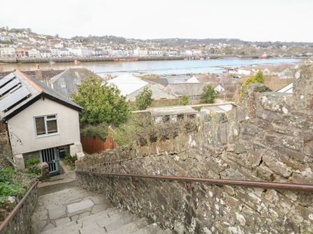 A stone stairway with metal railings leading down past a house with solar panels and a river with boats and houses in the background at Springfield Cottage in Bideford