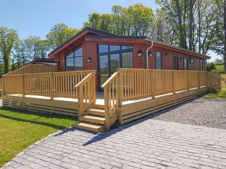 A wooden cabin with large windows and a surrounding wooden deck with railing at Wren Lodge in Gargrave