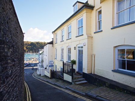 A narrow street with yellow brick buildings and a view of boats on the water at 11 Ridge Hill in Dartmouth