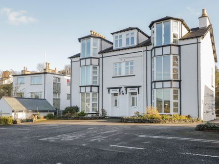 A white multi-story building with large bay windows and two entrance doors with a parking area in front at Tethera Bowness-On-Windermere