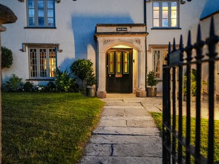 Exterior view of a house entrance with lit doorway pathway lawn and potted plants at Bath House in Langport