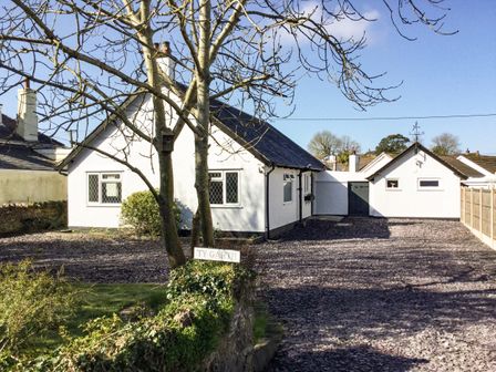 A white house with a shingle driveway and two leafless trees in front at Ty Garth in Benllech