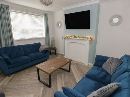 A living room with blue sofas and a coffee table at Cwtch Ar Y Mor in Burry Port