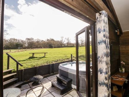 A patio with a hot tub and a small table and chair set opening onto a grassy field at Deer Lodge in Wimborne Minster