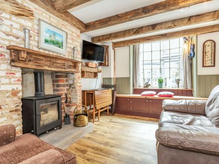 A living room with a wood burning stove a brown leather sofa a window seat with cushions and wooden ceiling beams at 48 High Street in Bridlington