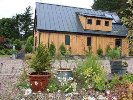 A wooden house with a metal roof surrounded by plants and flower pots at Larchwood Lodge in Ellon