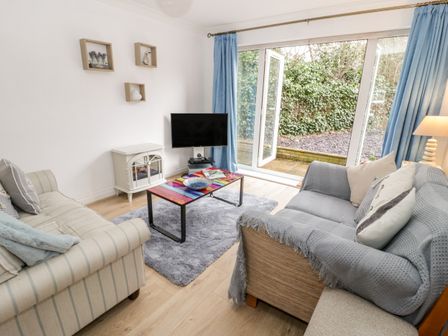 A living room with two sofas a colorful coffee table a TV and large windows with blue curtains at 10 The Orchard in Rhos-On-Sea
