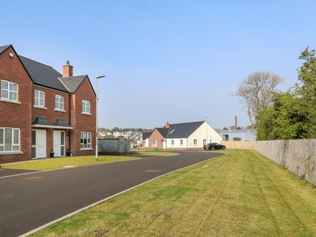 A paved road with brick and white houses on the left and right side with a lawn and wooden fence at Culmore Point Culmore Londonderry