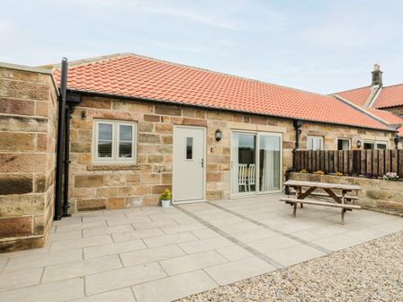 An outdoor patio area with stone walls a wooden picnic table and sliding glass doors at Cartwheel Cottage at Broadings Farm in Whitby