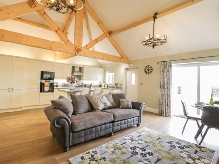 An open plan living room and kitchen with wooden beams a gray sofa a floral rug and a dining table at Abbey View Cottage at Broadings Farm in Whitby
