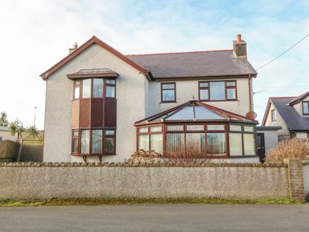 A two-story house with bay windows and a glass conservatory behind a low wall at Rhiangwyn in Llanrhyddlad near Cemaes Bay