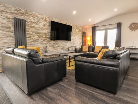 A living room with black leather sofas and yellow cushions facing a wall mounted TV at Box Tree Escapes in Kirkby Lonsdale